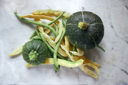 A still life composition showcasing fresh green and yellow squash with assorted beans on a marble surface.