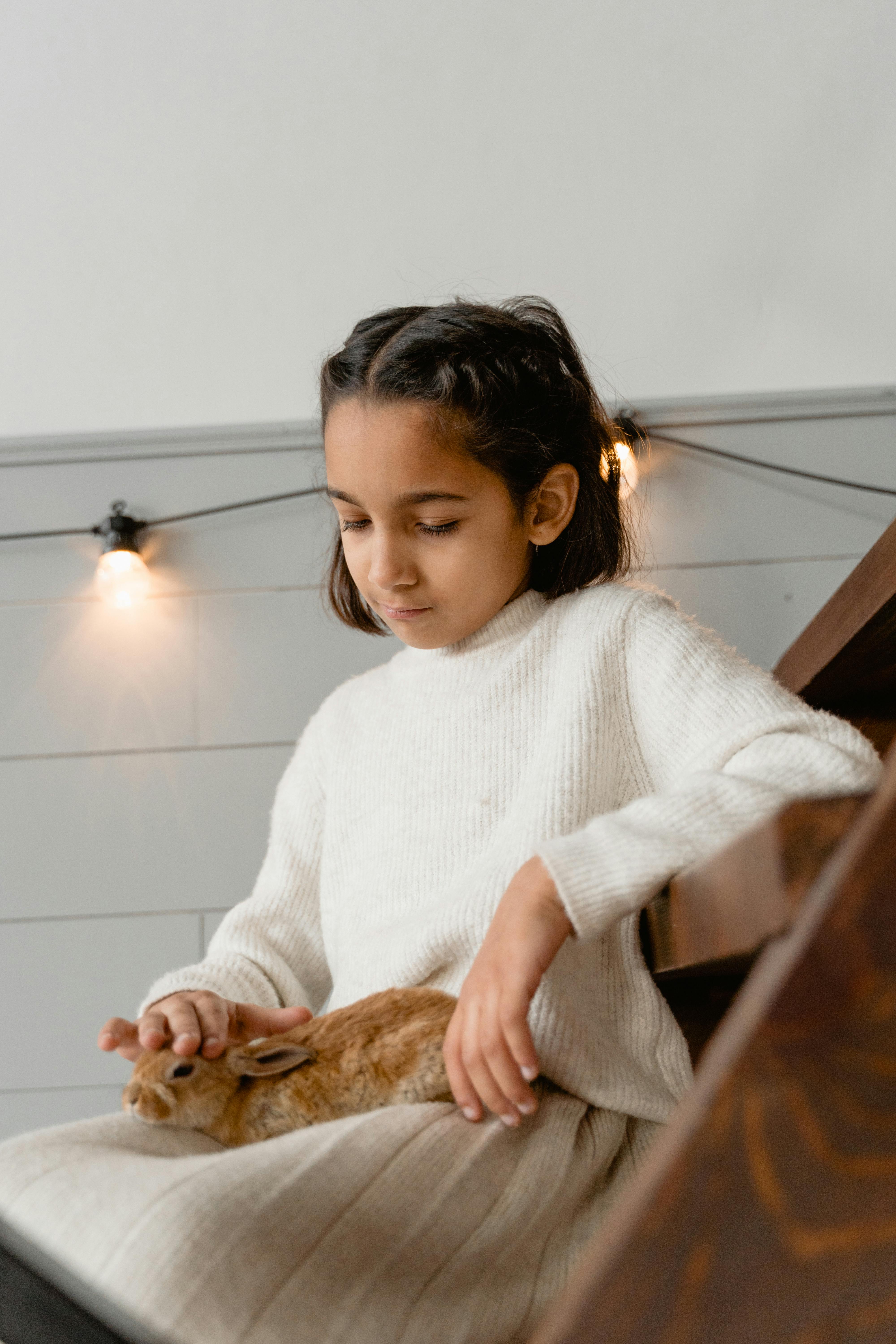 a girl sitting on a wooden stairs petting a rabbit