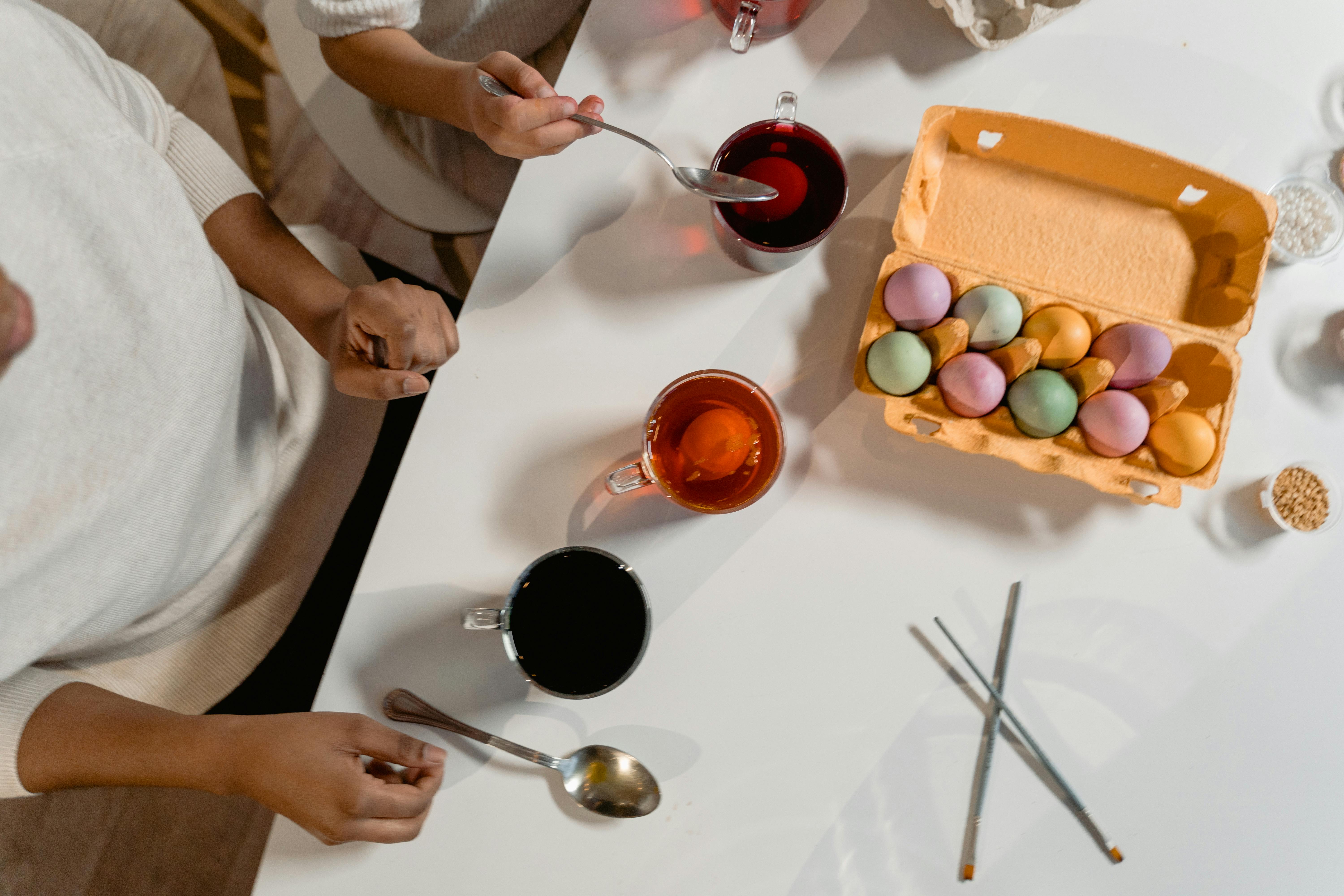 Top view of people coloring Easter eggs with various dyes on a table.
