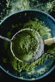 Green tea matcha powder in a sieve placed over a bowl, illustrating a healthy organic lifestyle.