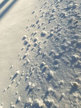 Close-up of textured snow with long shadows creating an abstract winter scene.