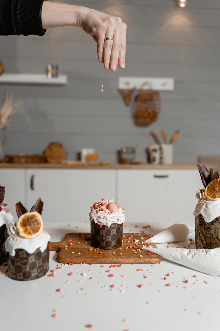 A Person Dropping Sprinkles On A Cupcake