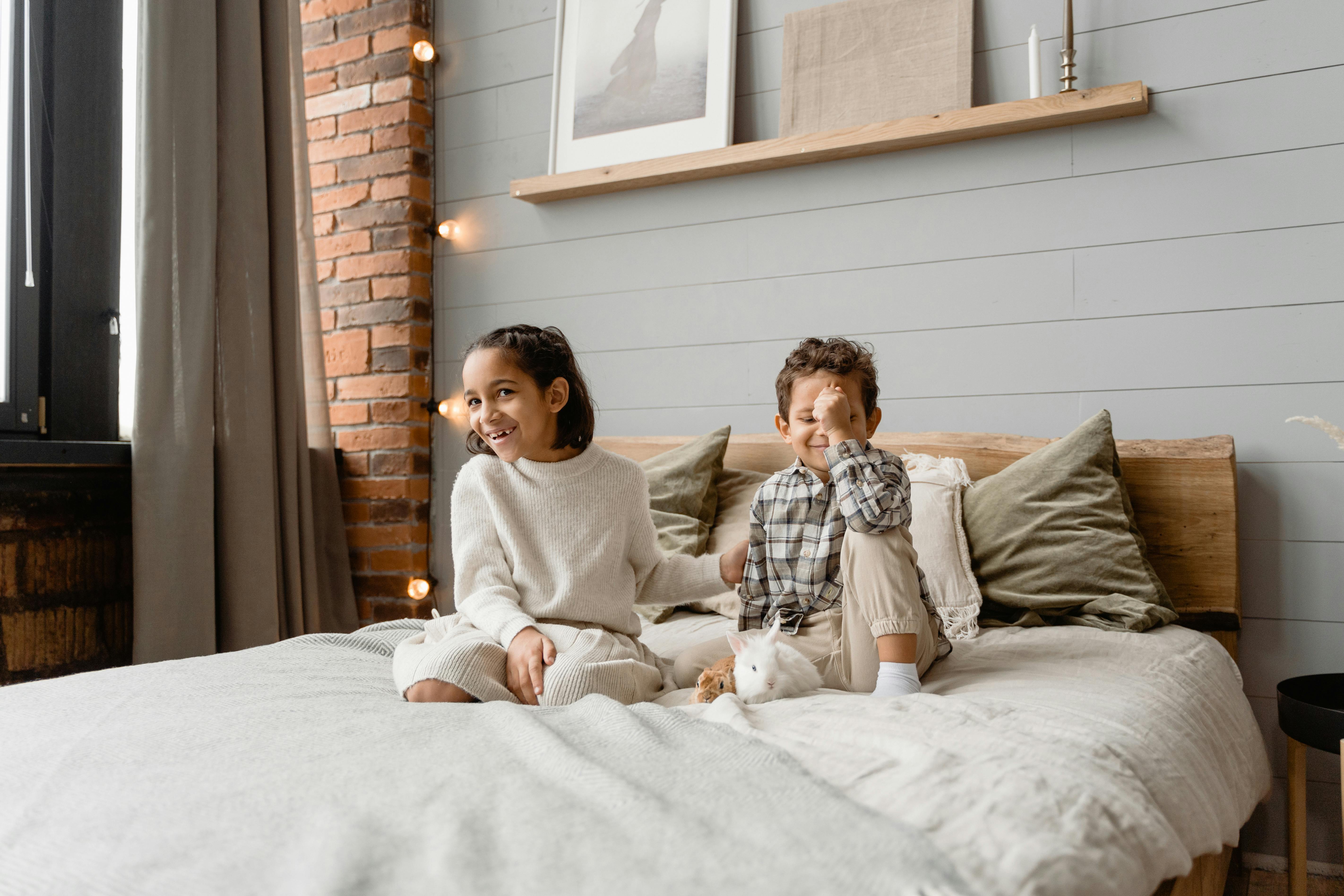 a girl and a boy sitting on bed with a rabbit