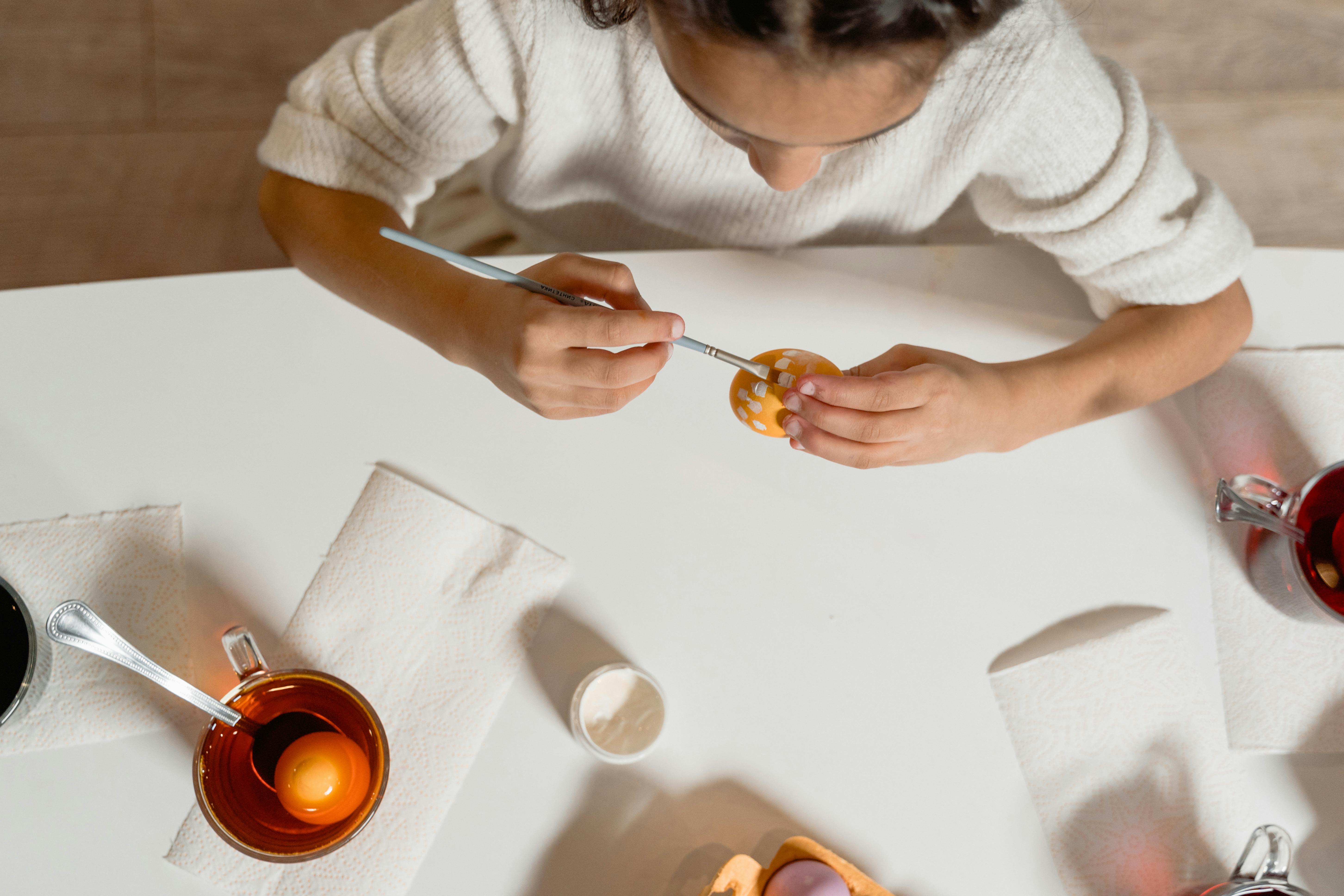 A child painting an Easter egg with a brush, focused on creative arts and crafts indoors.