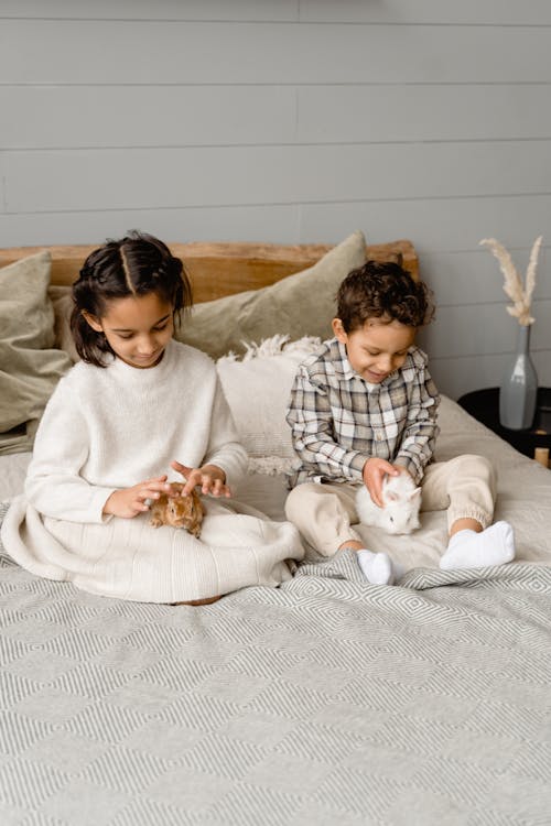 A Girl and a Boy Siting on Bed with Rabbits