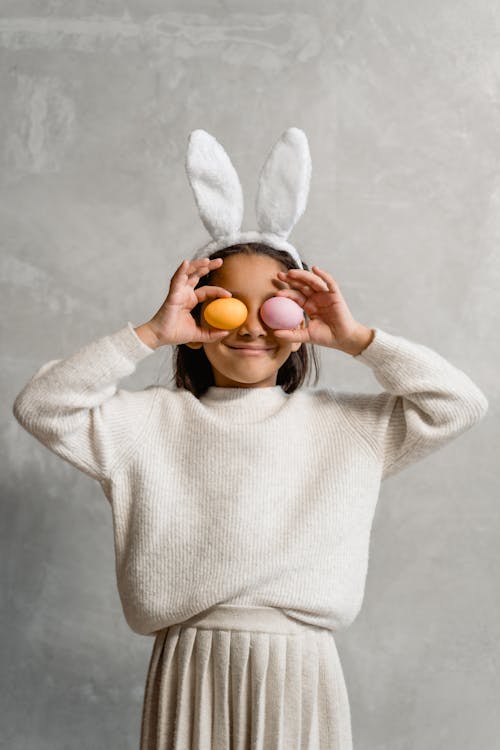 Girl wearing Easter bunny Headwear covering her Eyes with Easter Eggs