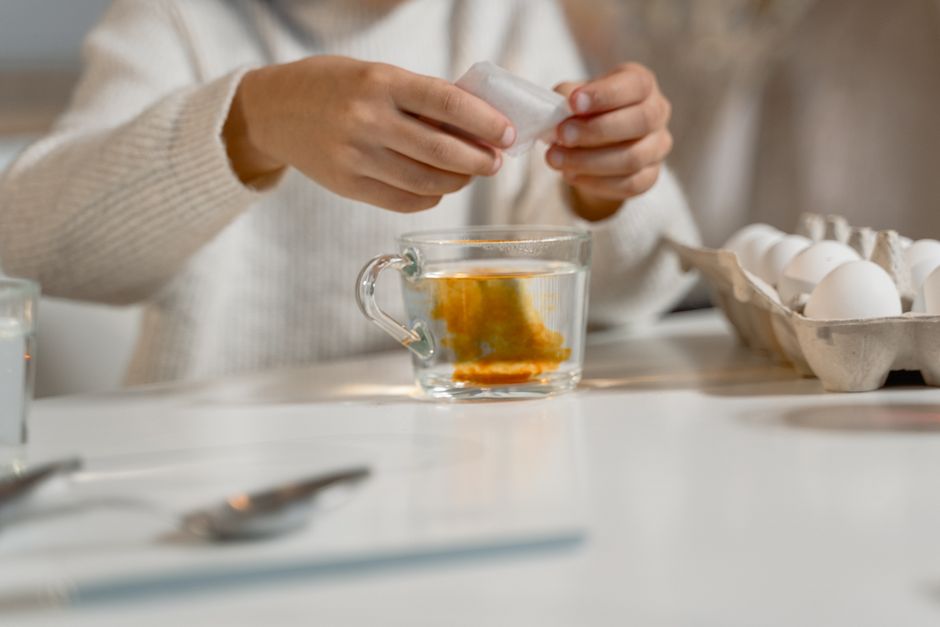 Close-up of hands dyeing eggs with natural colors, in a cozy indoor setting.