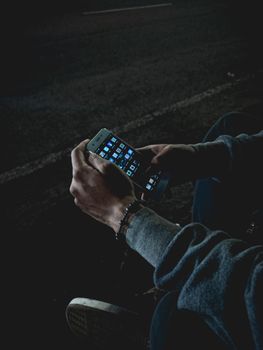A person using a smartphone on a dimly lit street, highlighting nightlife tech usage.