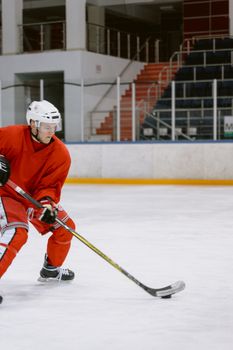 A hockey player in red gear skates with focus on the ice rink indoors.