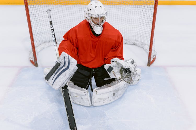 Man In Red And White Hockey Jersey And Helmet Sitting On Ice Field
