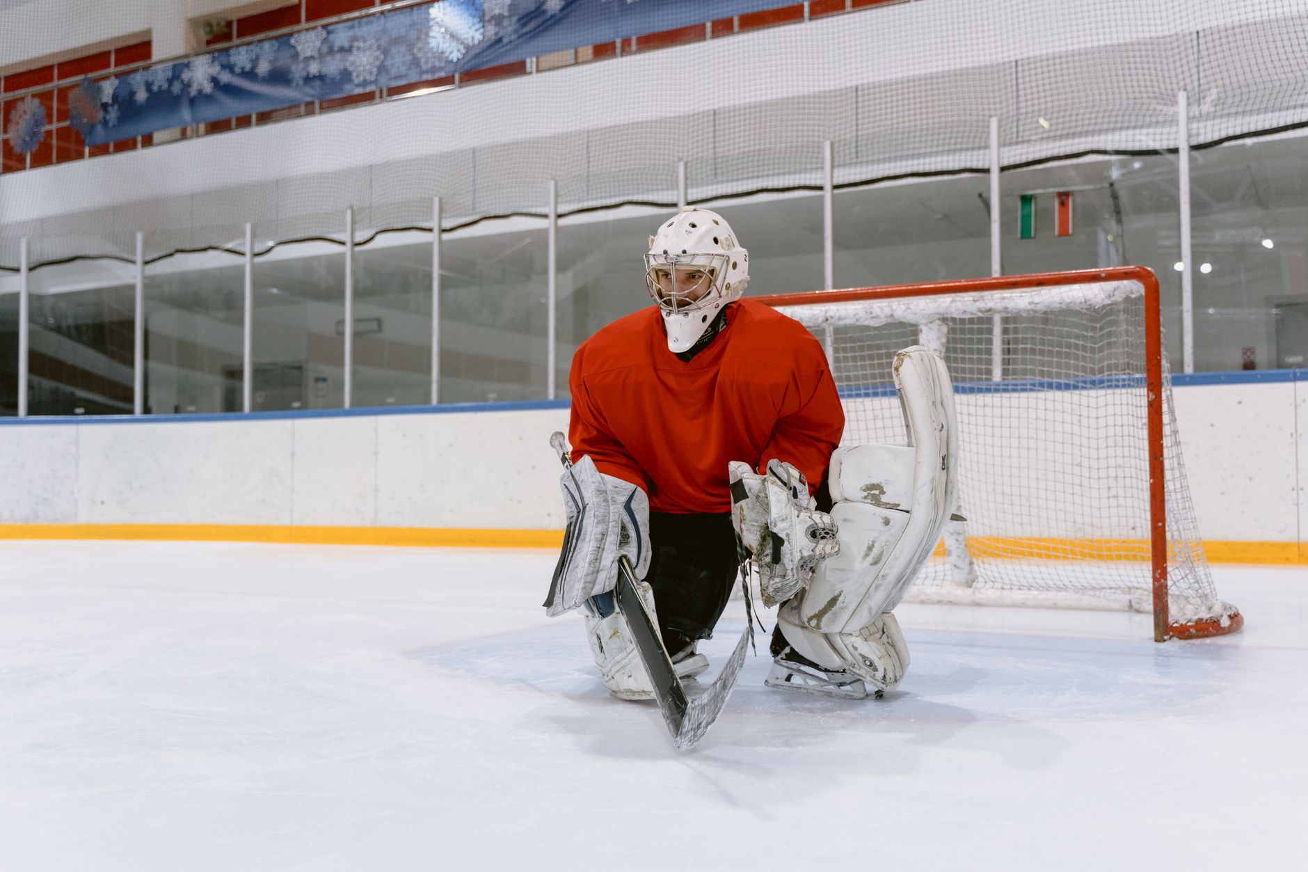 Ice hockey goaltender in red jersey at the rink, ready to defend the goal.