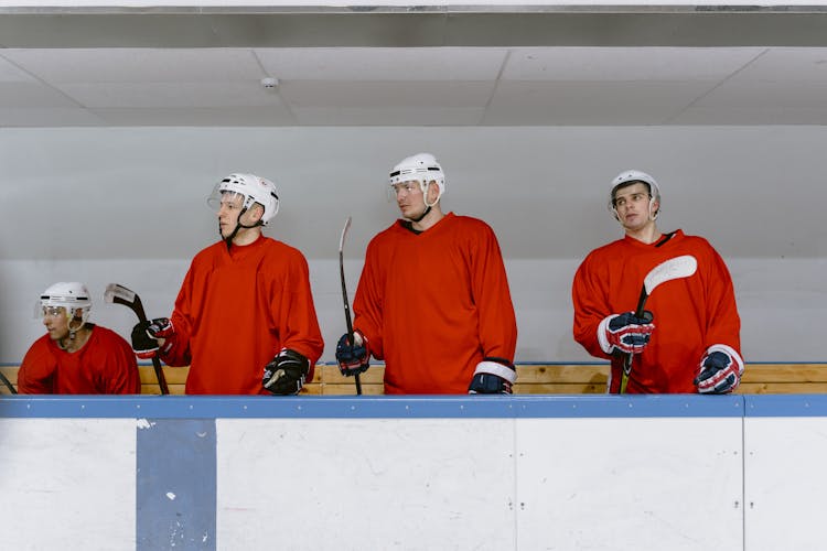 Men In Red Hockey Uniforms Standing Behind The Hockey Rink 