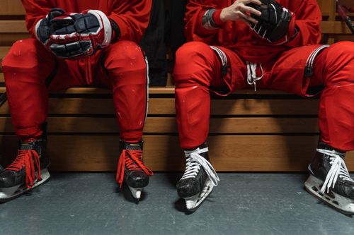 Free Two hockey players in red uniforms sitting on a bench, wearing skates and gloves indoors. Stock Photo