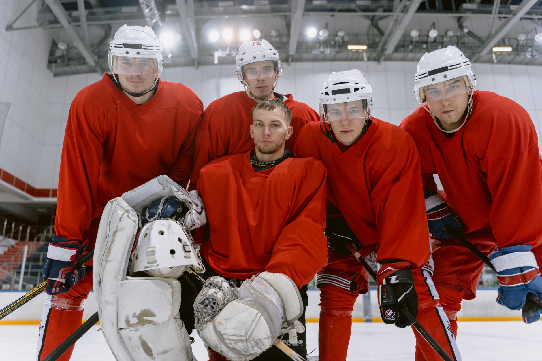 Group of male hockey players in red uniforms, ready on the ice rink indoors.