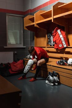 Male athlete adjusting protective gear in a locker room setting, preparing for sports.