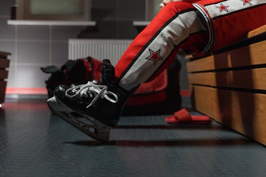 Close-up of a hockey player in red gear resting on a wooden bench with ice skates.