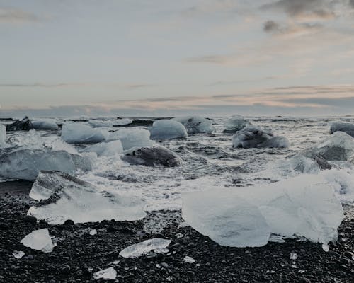 White big ice pieces on wet seashore near rippling water against cloudy sky in nature in winter day on cold weather