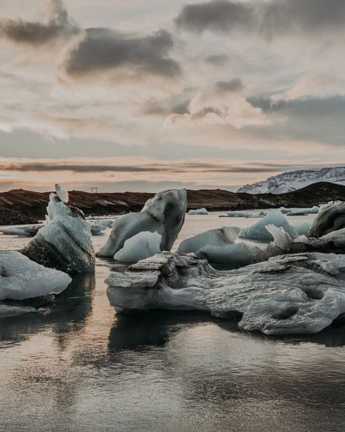Free Big white ice pieces near calm water of sea against cloudy sky and hilly area in nature on cold winter day Stock Photo