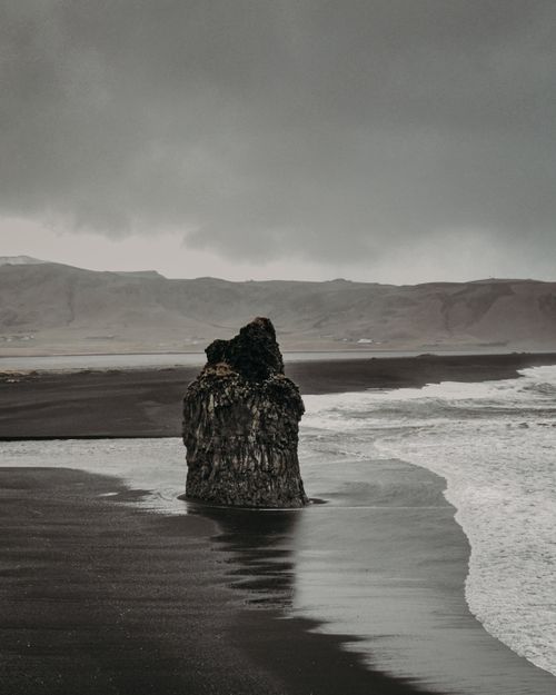 Free Stony formation on sandy coast near rippling foamy water of sea against overcast sky and hilly area in wild nature Stock Photo
