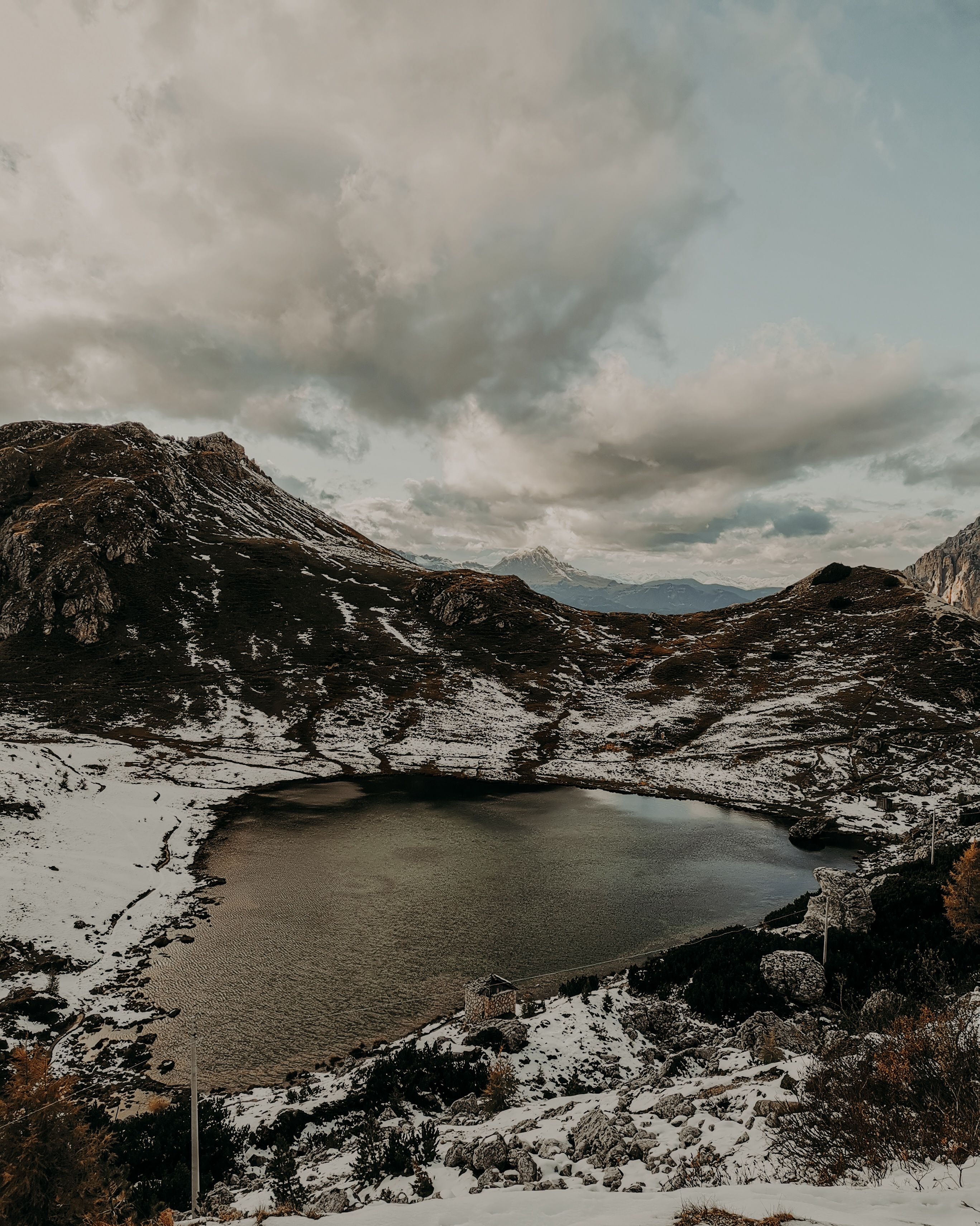 Small lake with calm frozen water surrounded by snowy rocky formations against cloudy sky in nature on cold winter day