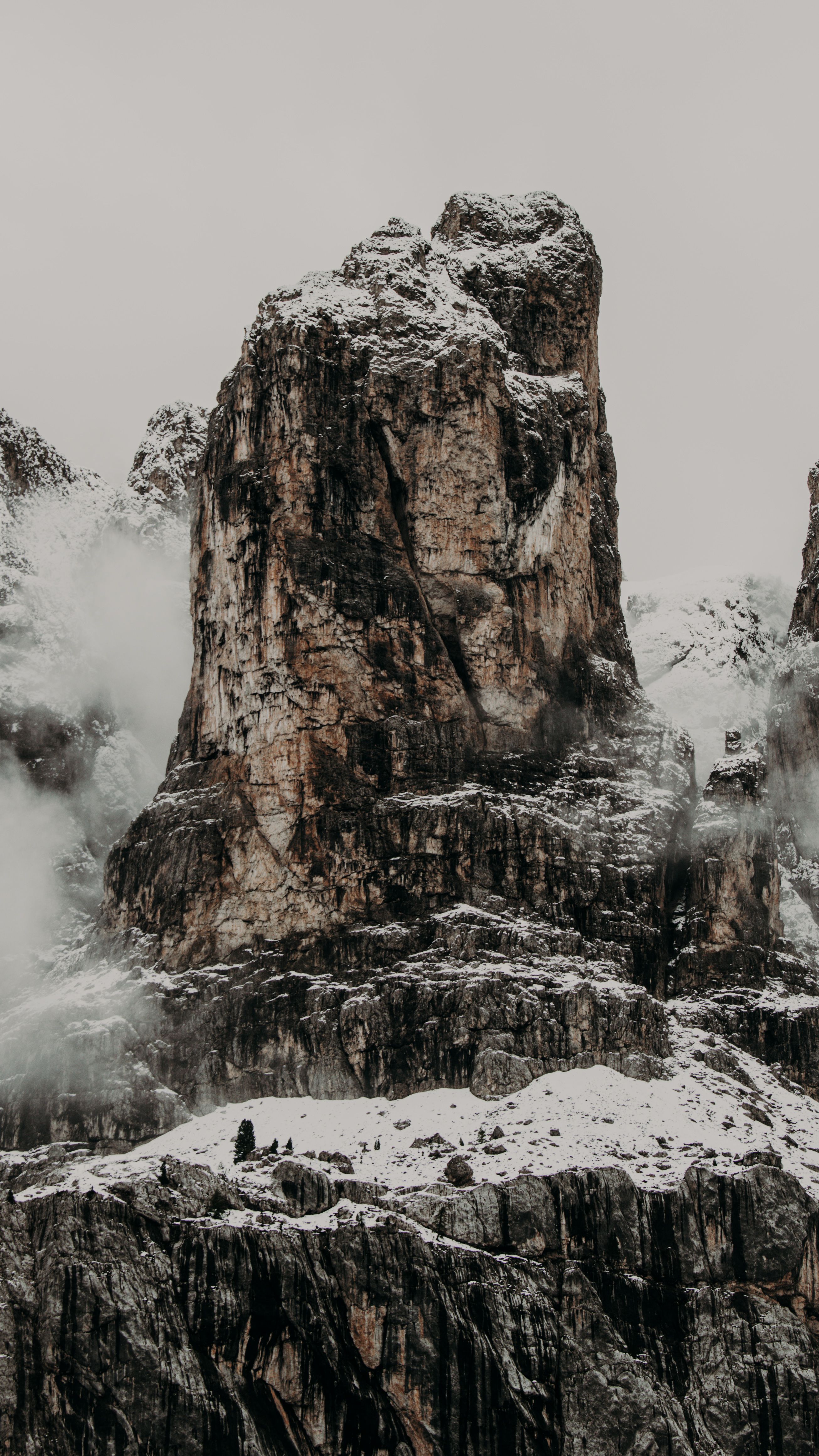 Tall rough rocky cliffs with uneven surface covered with snow against cloudless sky in foggy weather on cold winter day