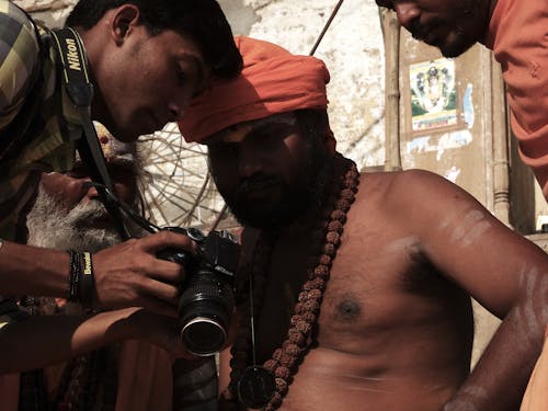 A Photographer and Shirtless Man Wearing a Beaded Necklace 