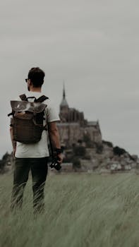 A man with a backpack and camera overlooks Mont Saint-Michel on a misty day.