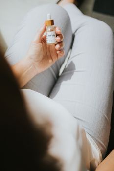A close-up of a hand holding a skincare dropper bottle, conveying a relaxed lifestyle vibe.