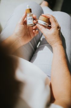 A woman holds skincare products in natural light, focusing on self-care.