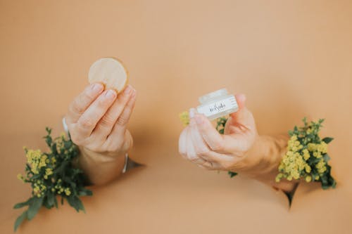 Hands Breaking Through the Paper Wall Holding a Container with Face Cream 