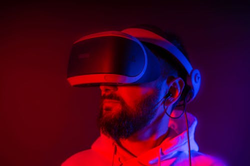 Young bearded man entertaining with VR glasses in colorful neon light on black background