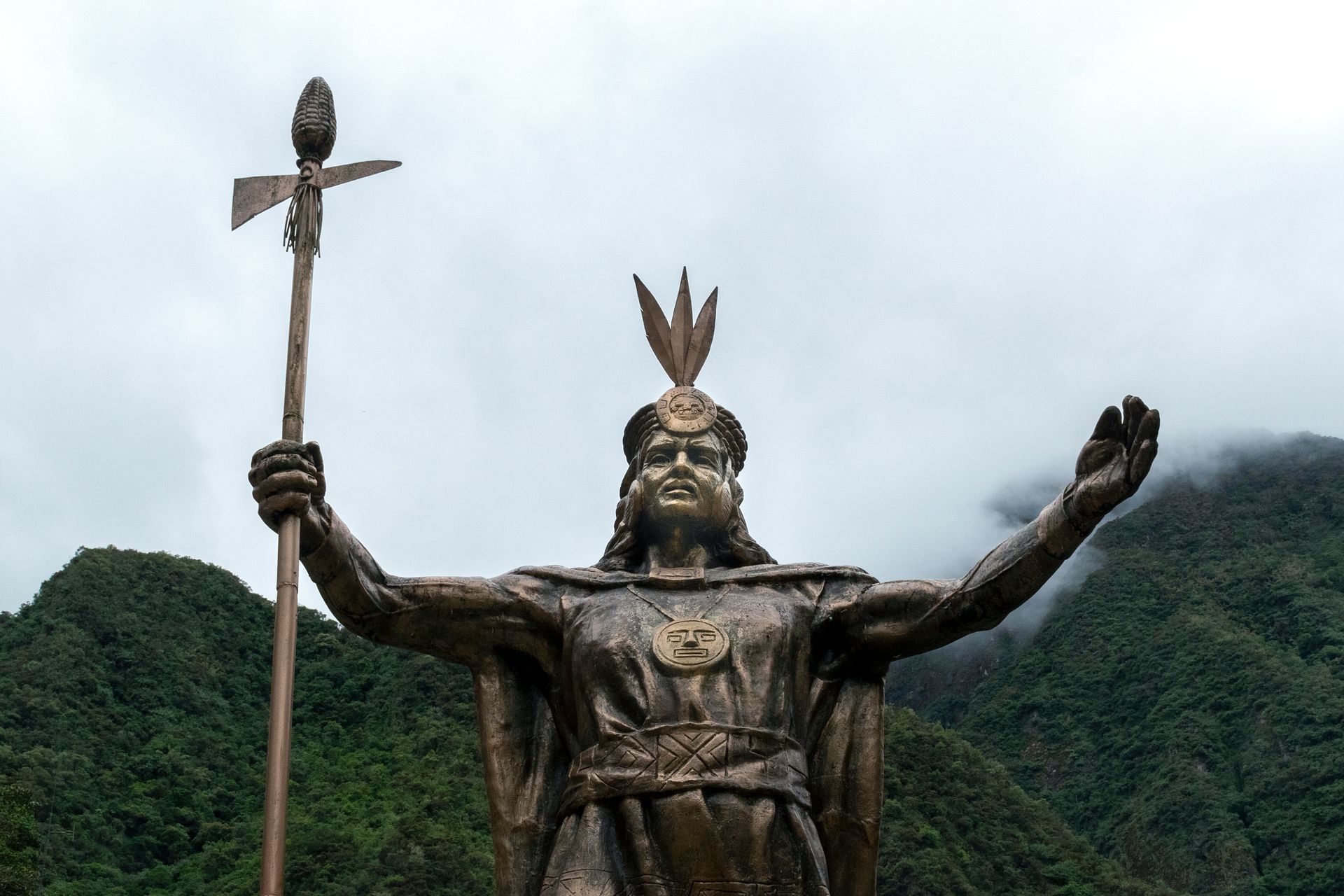 Majestic statue of an Incan warrior in Aguas Calientes, Peru against mountain backdrop.