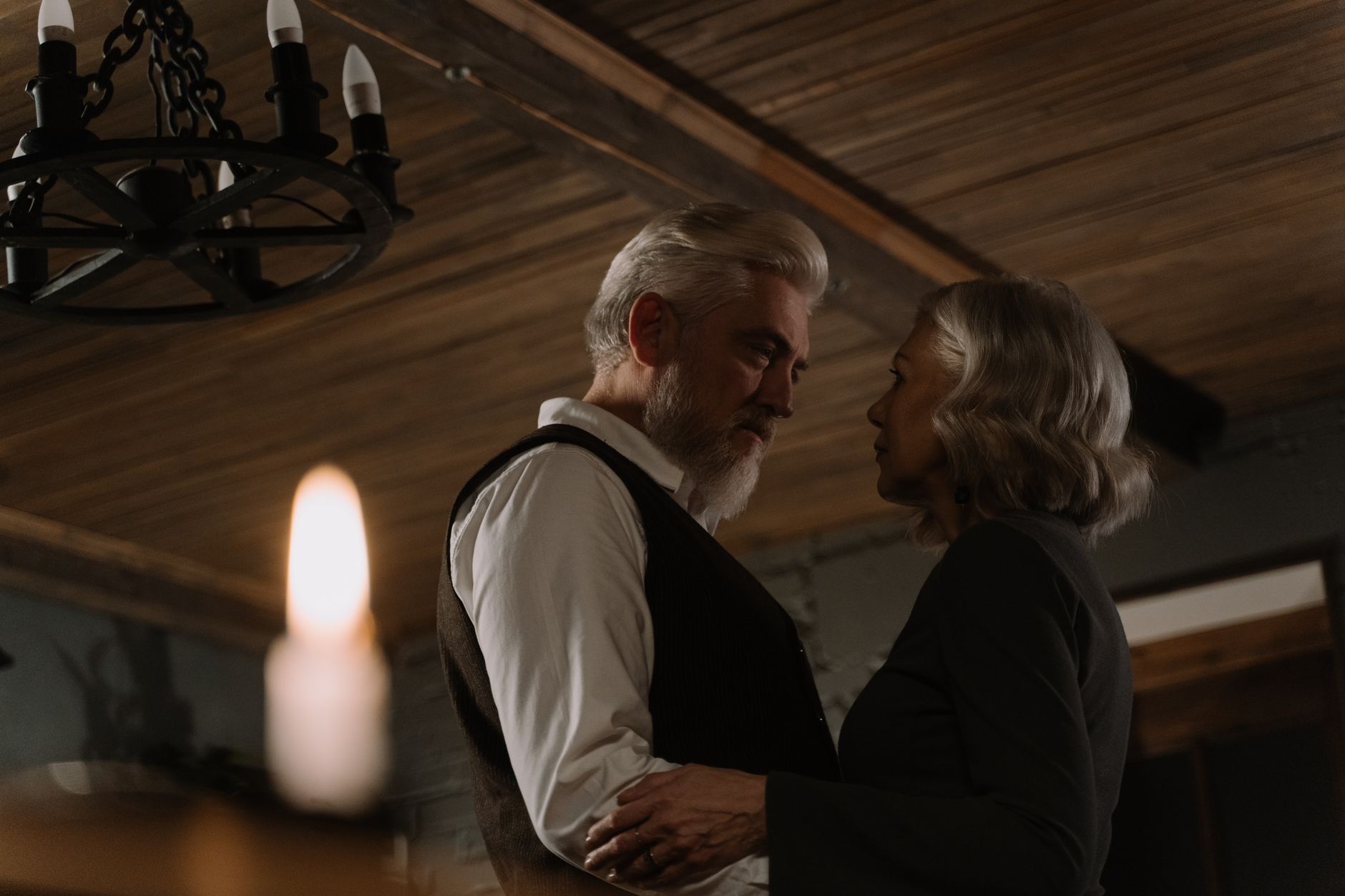 A senior couple shares a romantic dance in a warmly lit room.