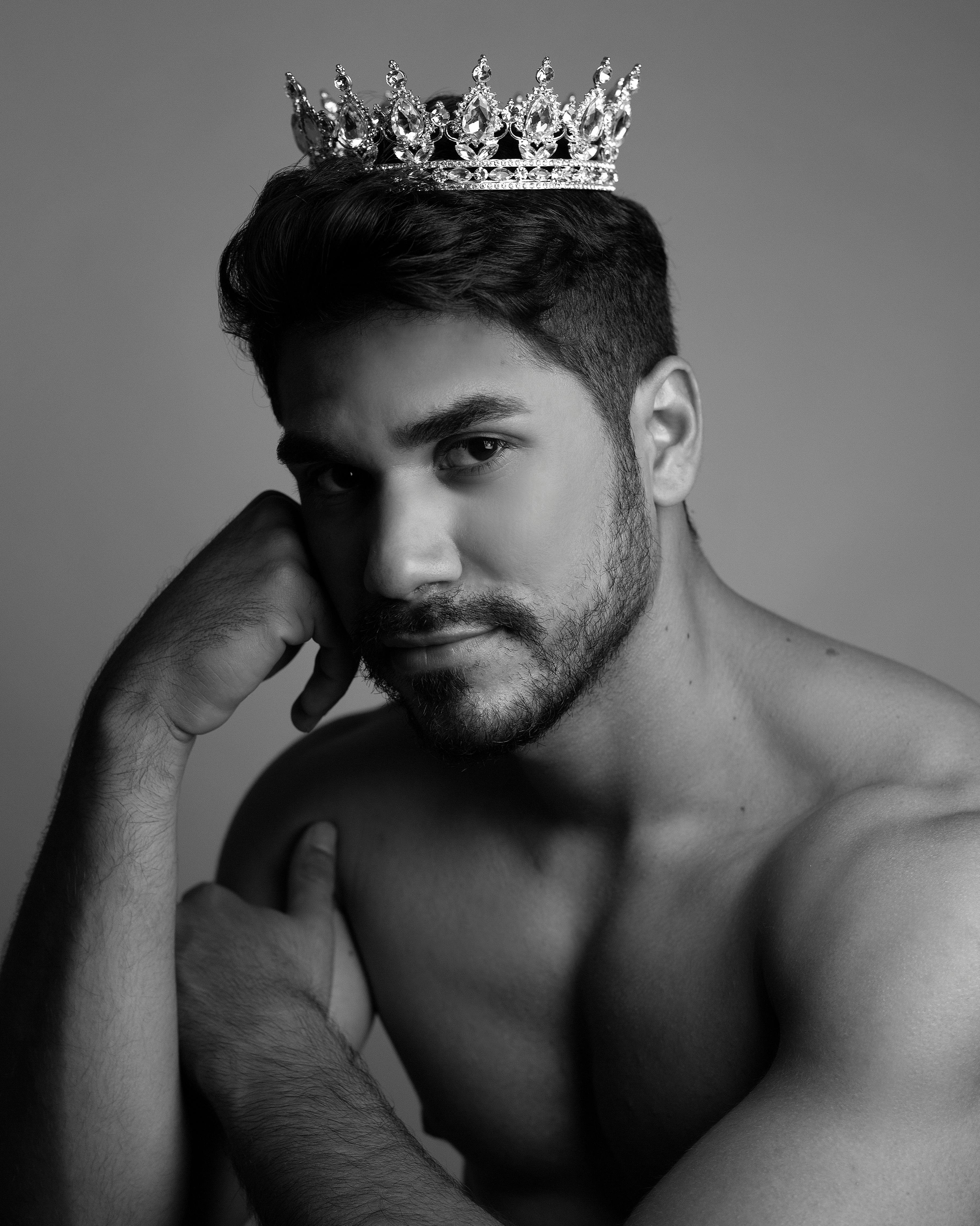 masculine shirtless ethnic man with crown on head looking at camera