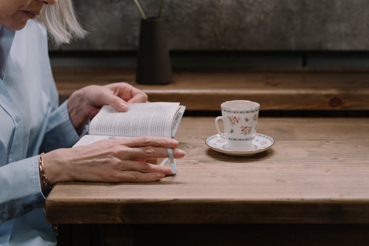 A Person Reading Book Over A Dinner Table