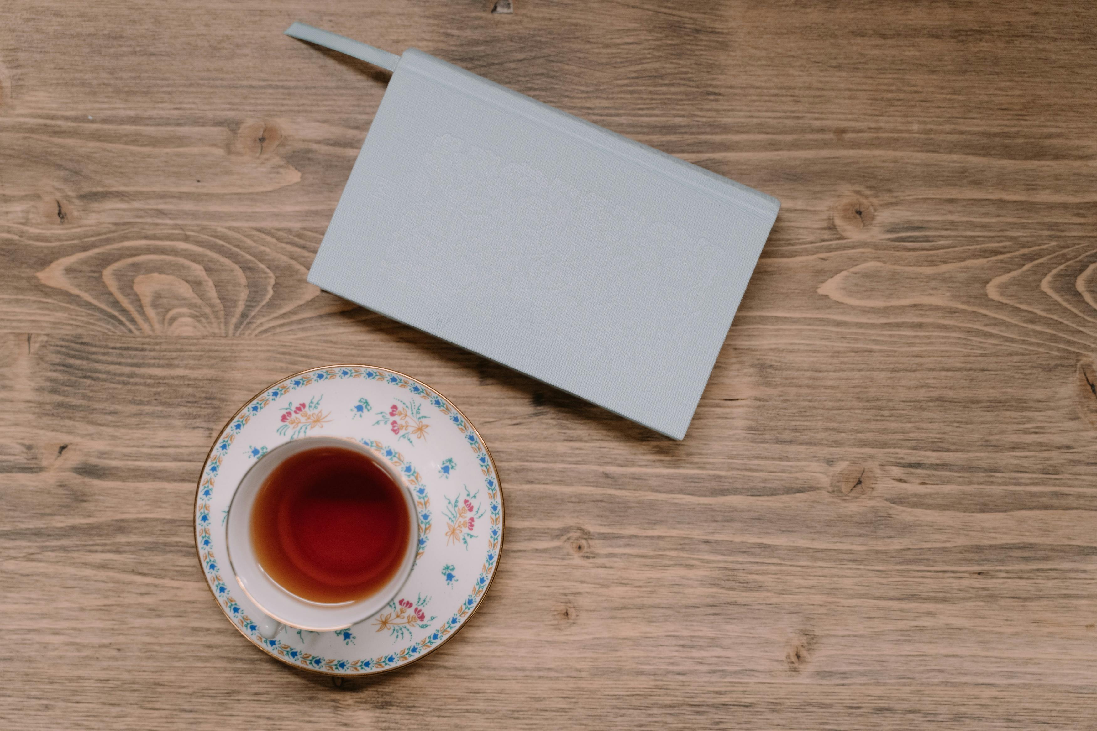 A calming flat lay featuring a cup of tea and a notebook on a wooden surface, ideal for study or relaxation themes.
