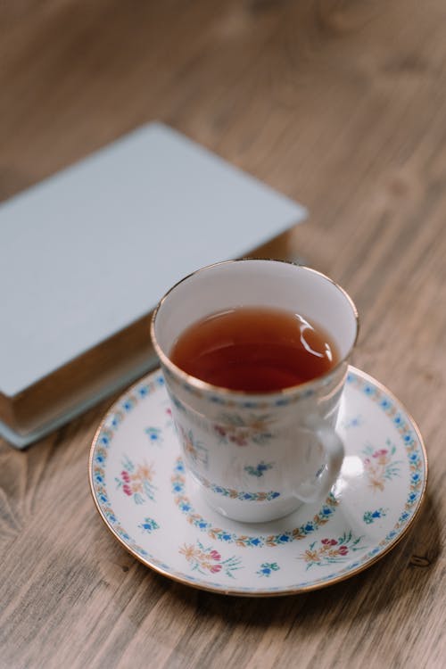 Close-Up Shot of a Cup of Tea beside a Book on a Wooden Surface