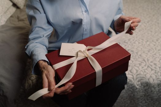 A person opens a red gift box wrapped with a white ribbon indoors, creating a warm and personal moment.