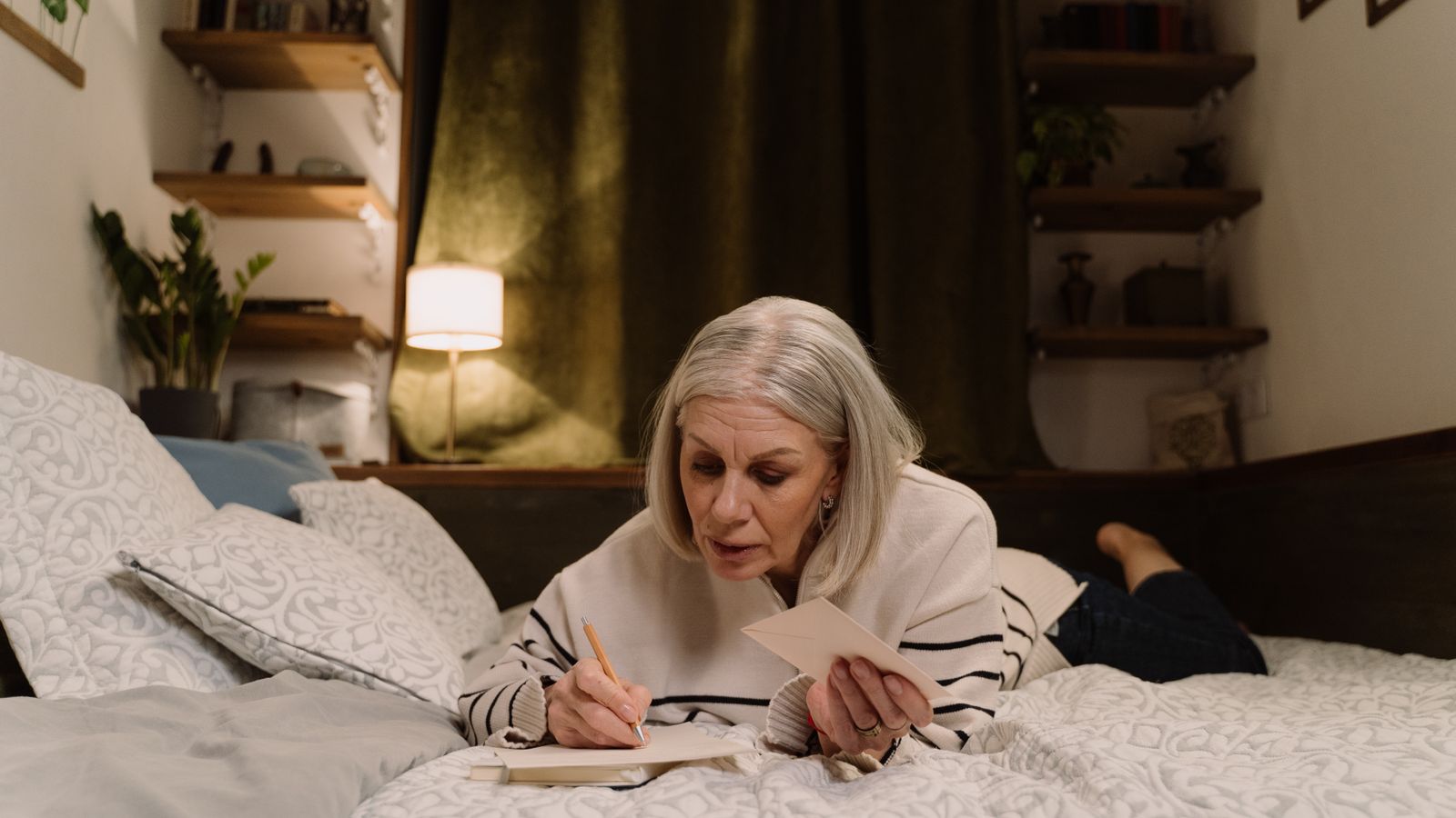 A person writing in a notebook and holding an envelope