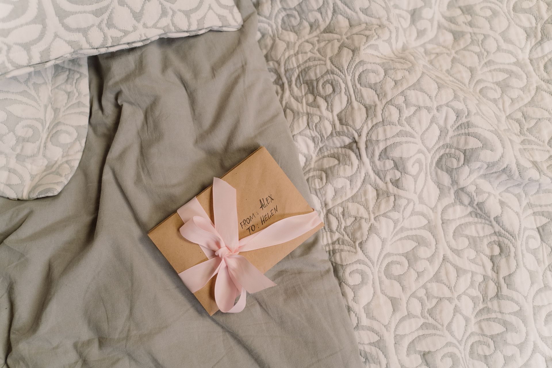 A close-up of a gift envelope with a pink ribbon, placed on elegant patterned bedding, adding a personal touch.