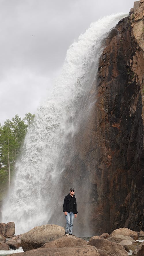 Man Standing on a Rock in front of a Waterfall 