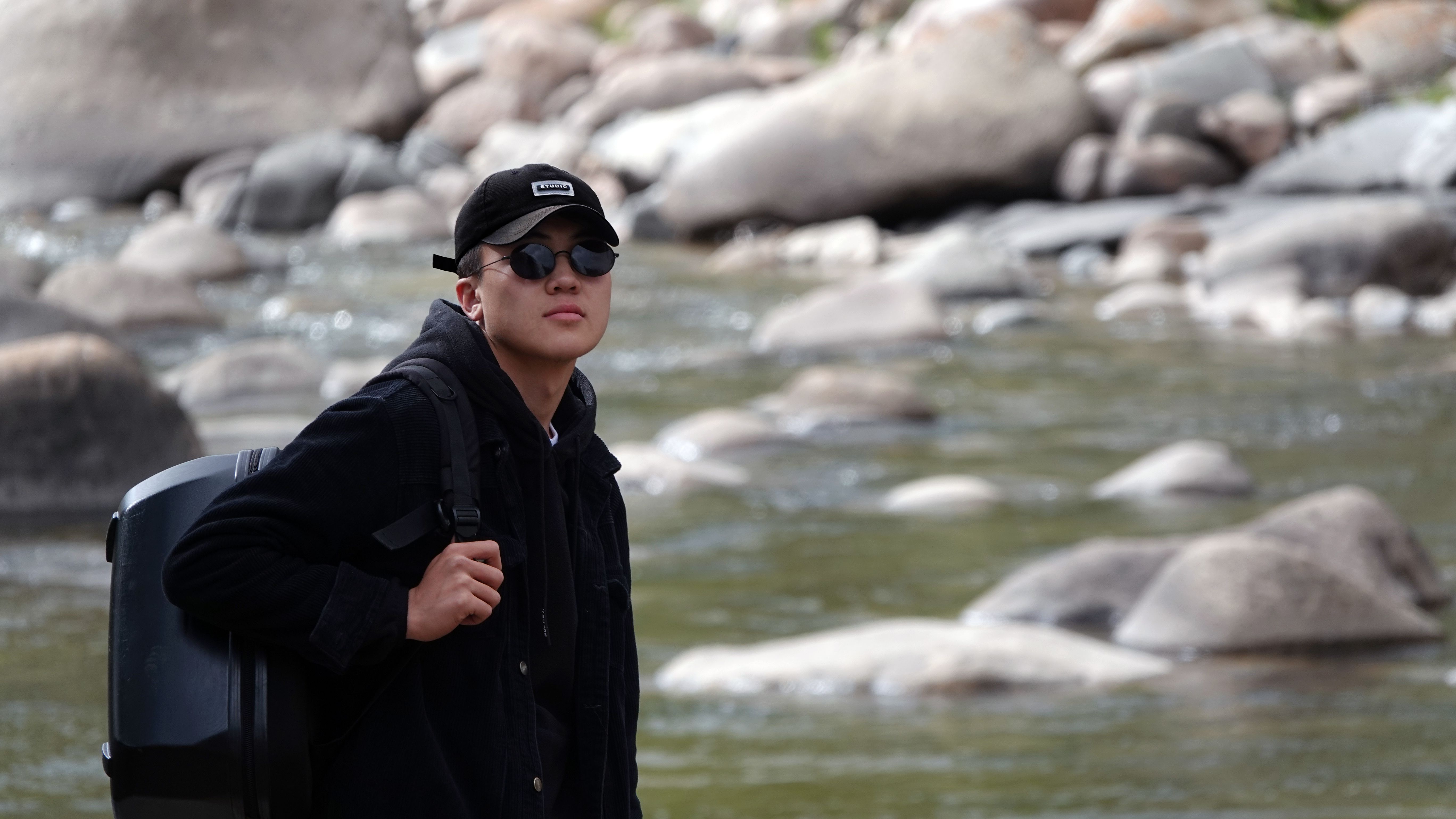 Portrait of a young man in Mongolia, standing beside a rocky river, exuding an adventurous spirit.