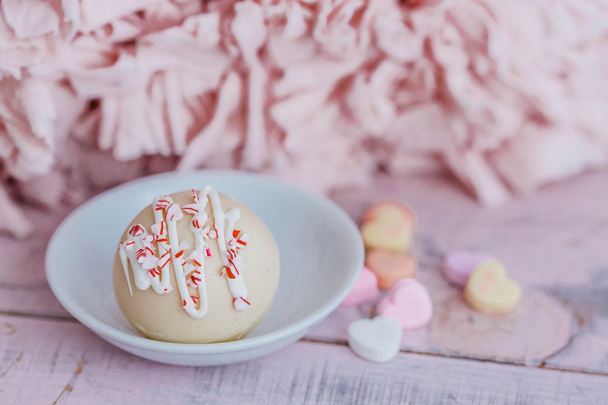 A delicious hot cocoa bomb with peppermint sprinkles, surrounded by heart-shaped candies, perfect for a sweet treat.