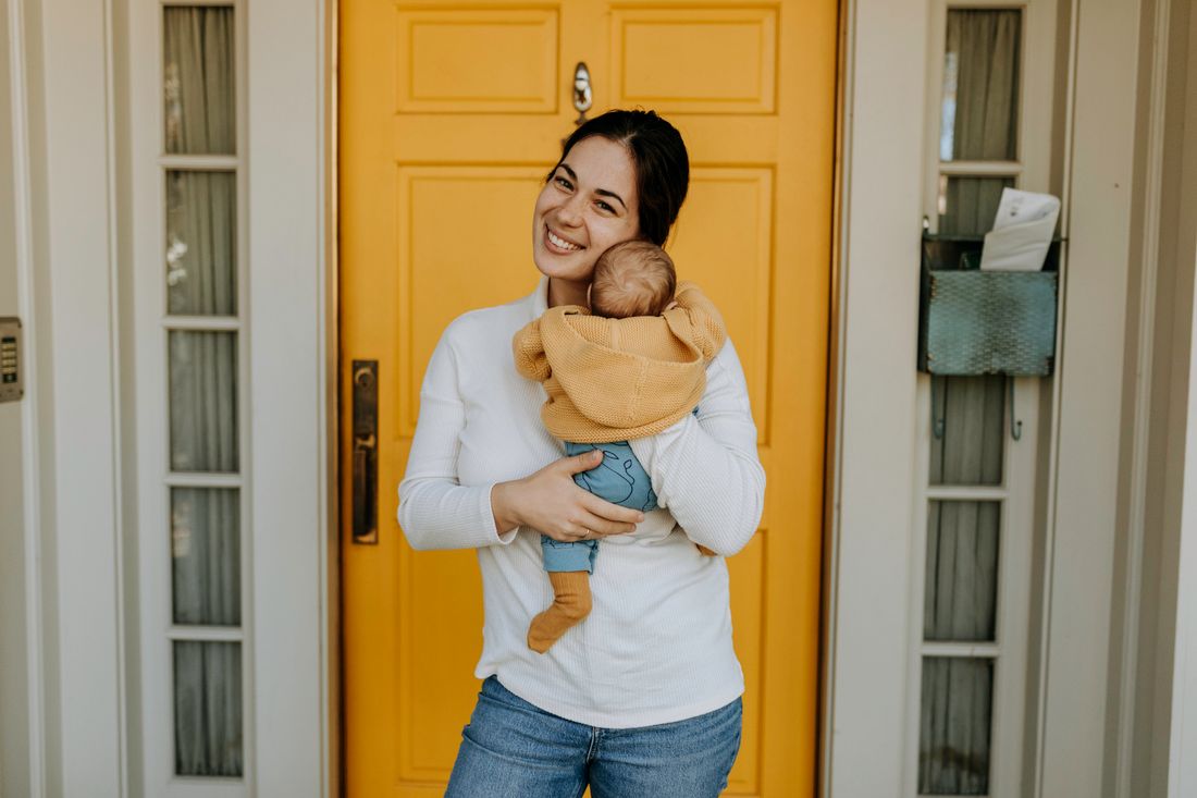 A smiling mother holding her baby at the front door