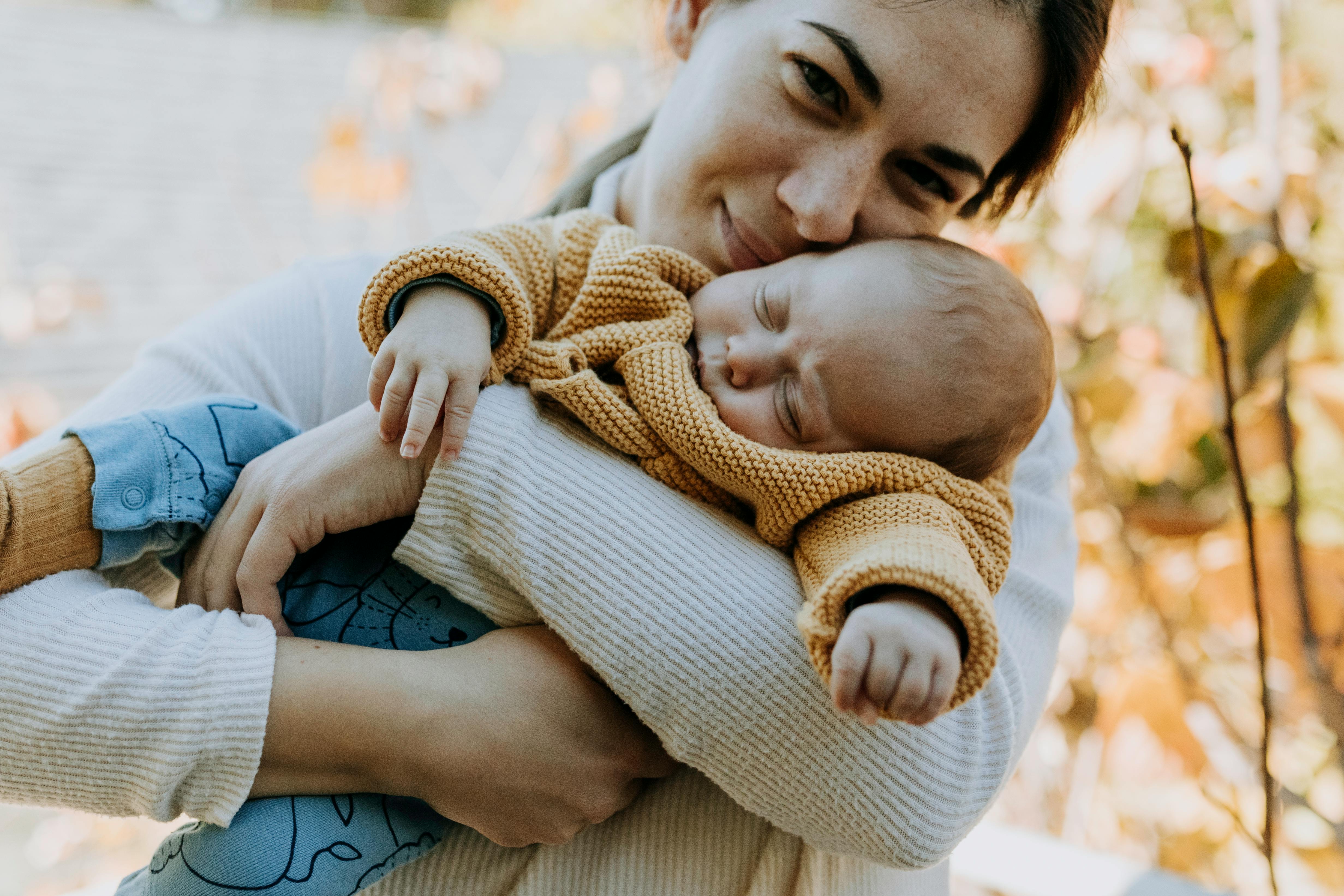 A tender moment of a mother hugging her sleeping baby in a cozy sweater outdoors.