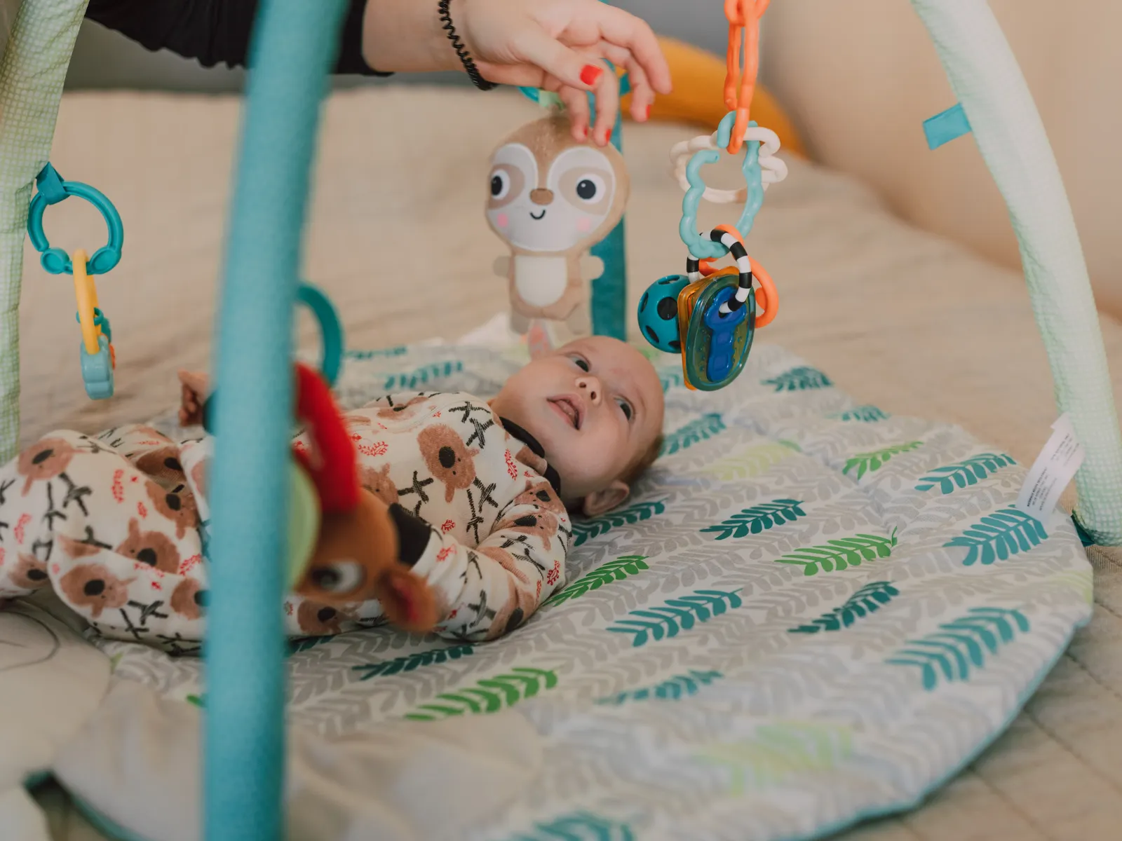 Baby in a onesie lying on a play mat, reaching for hanging toys
