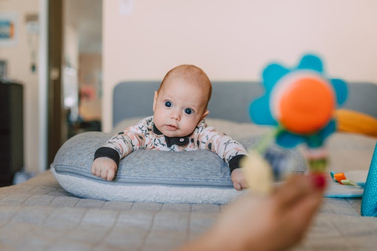 Baby Wearing Onesie Lying Down On A Grey Pillow