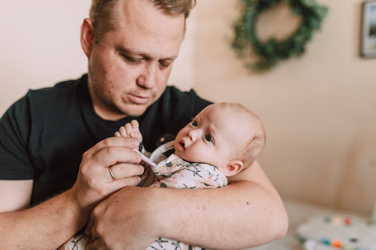 Man Using Thermometer To Check The Baby's Temperature