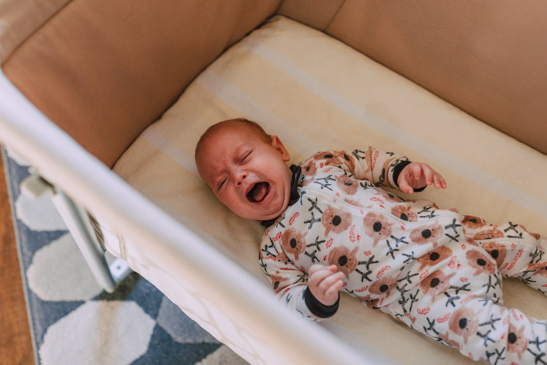 Free A Baby in Onesie Crying while Lying Down on Crib Stock Photo