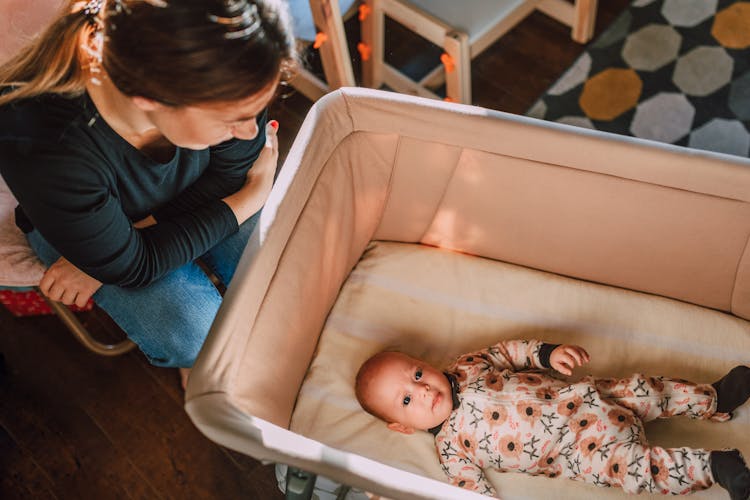 A Woman Sitting Beside A Baby In A Crib